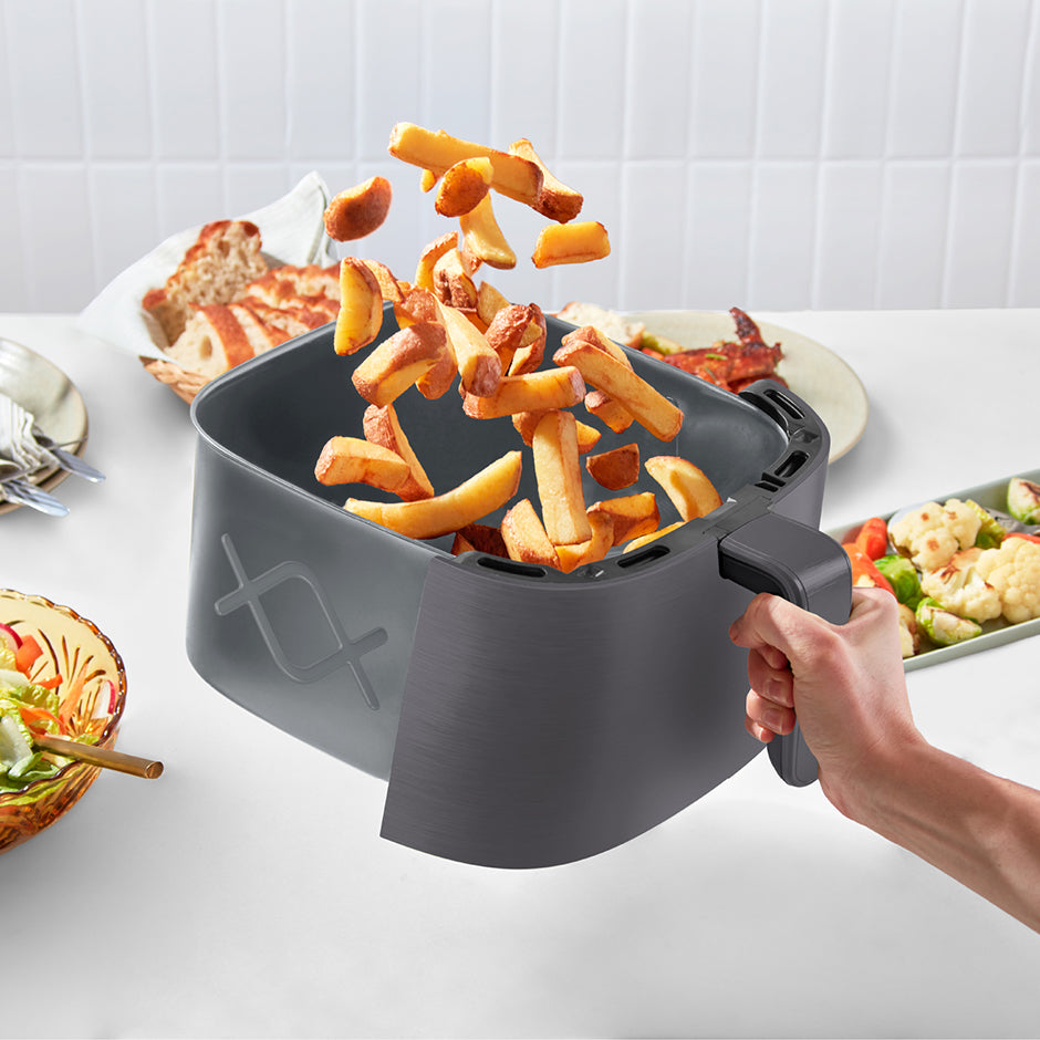 Person holding a portable fryer with fries on a kitchen counter