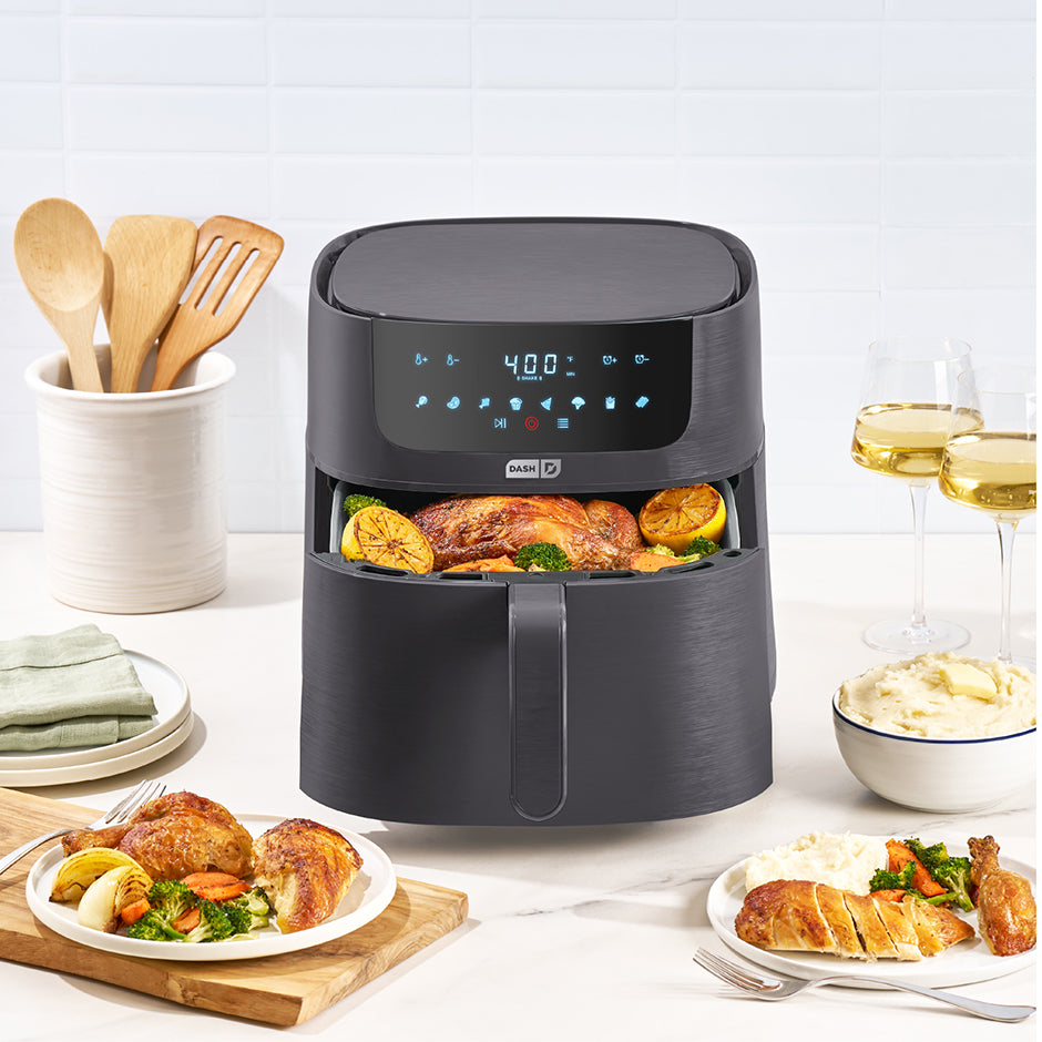 Black air fryer with cooked food on a table with plates and glasses.