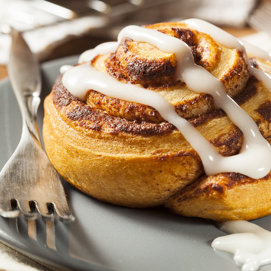 Cinnamon roll with white icing on a plate with a fork