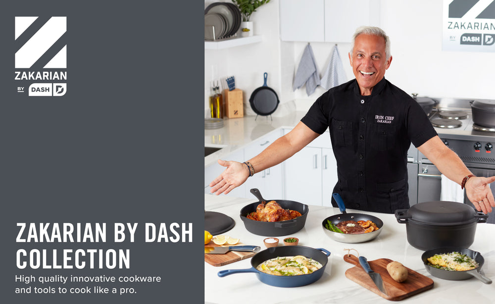 Geoffrey Zakarian in a kitchen wearing a black shirt gestures to the Zakarian by Dash collection on a white countertop. 