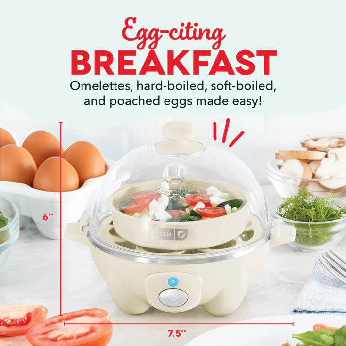 Cream-colored electric egg cooker with dome lid, surrounded by brown eggs, fresh vegetables, and bread on a kitchen counter.