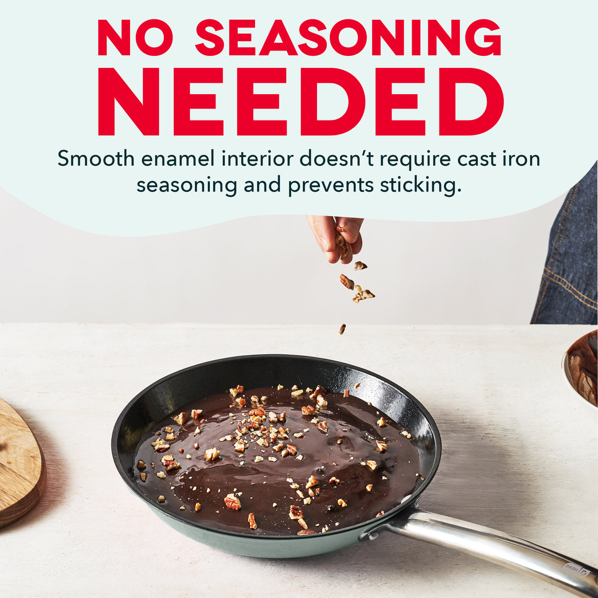 Teal cast iron skillet with smooth dark interior containing chocolate and nuts, hand sprinkling ingredients above.