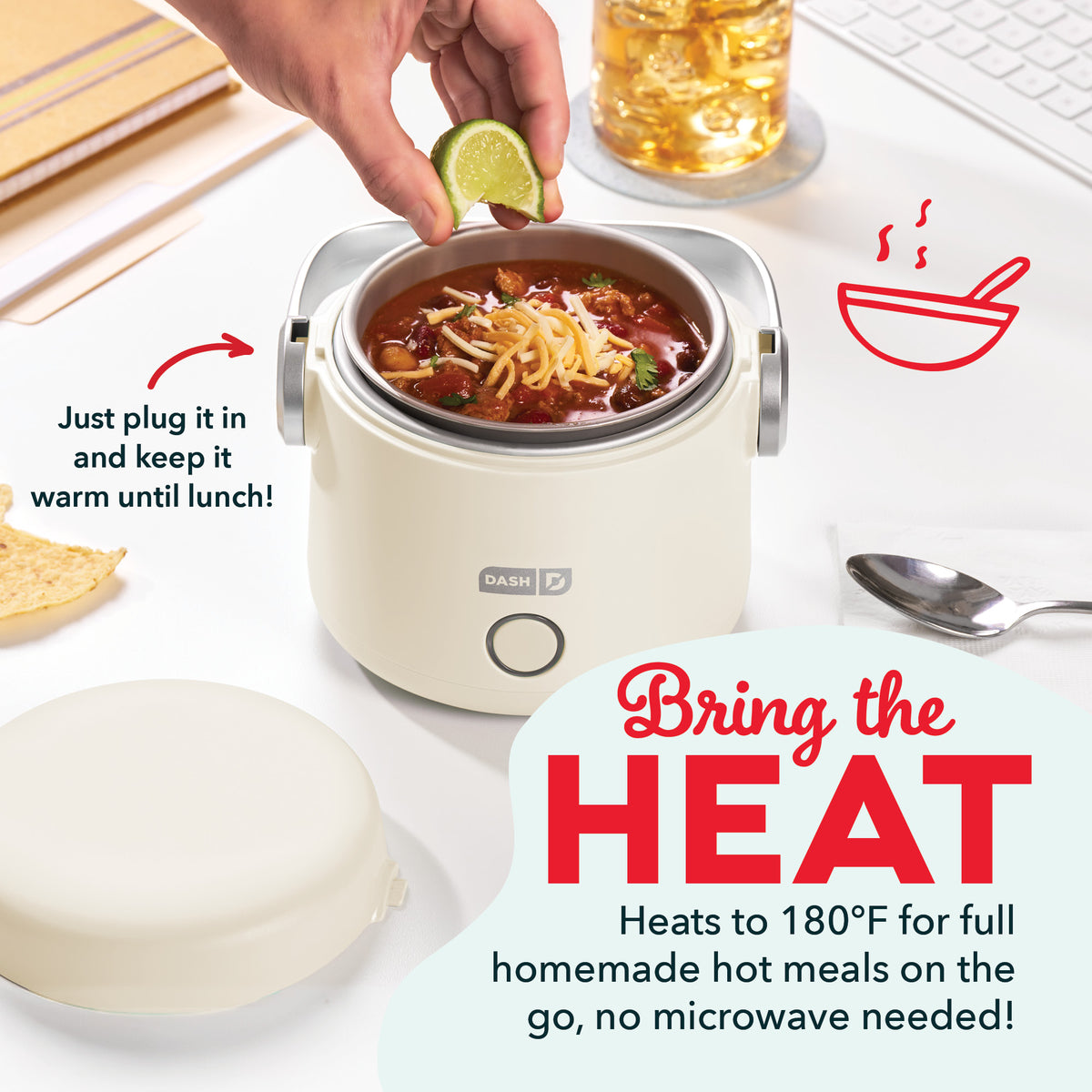 Cream-colored electric lunchbox with noodle soup inside, hand adding lime garnish, beverage and utensils nearby.