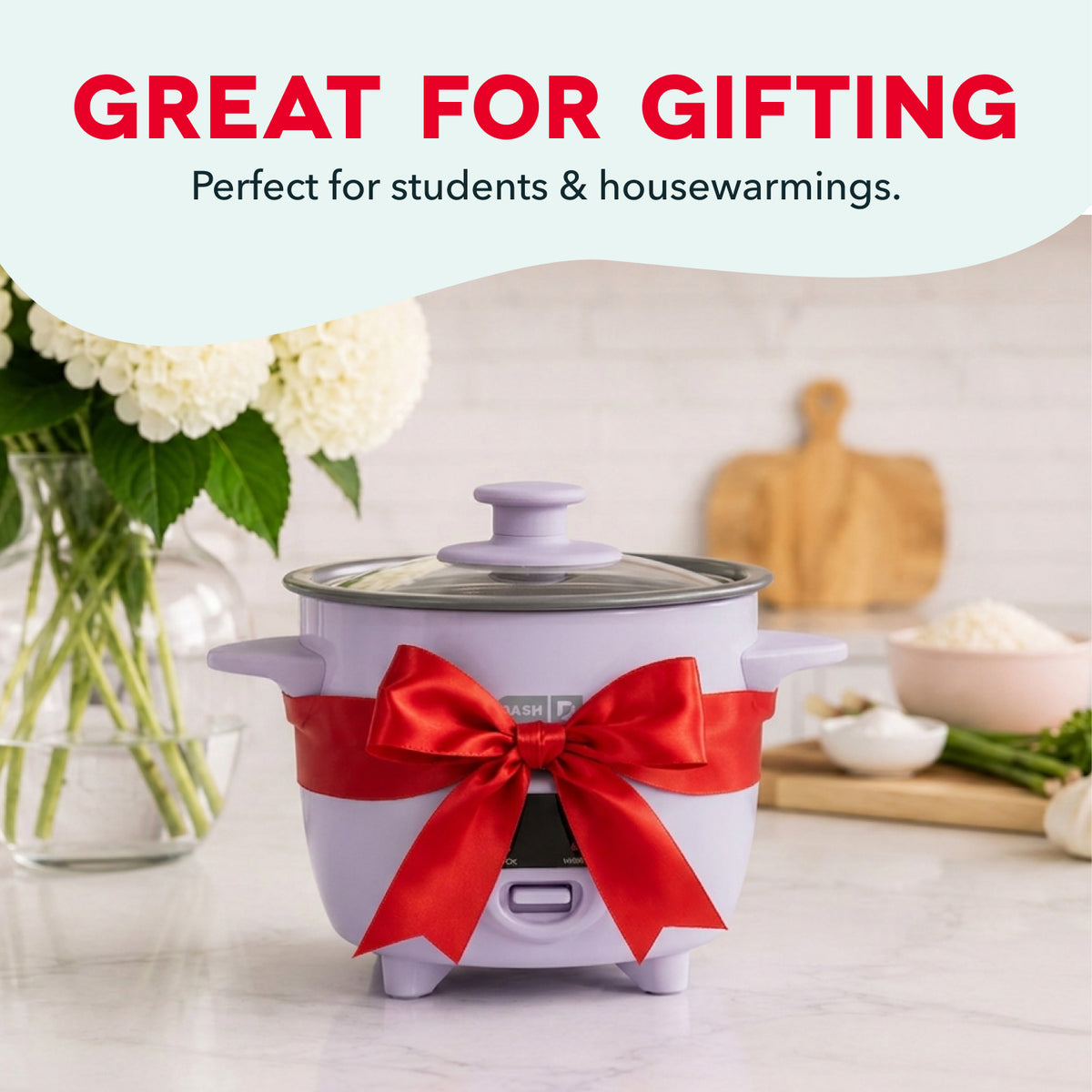 Compact lavender rice cooker with glass lid, red ribbon bow, and control panel on kitchen counter.