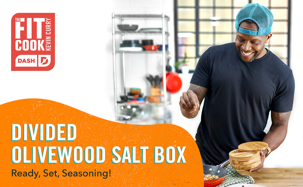 The Fit Cook Kevin Curry wears a black t-shirt and a blue backwards cap while sprinkling salt on a dish.