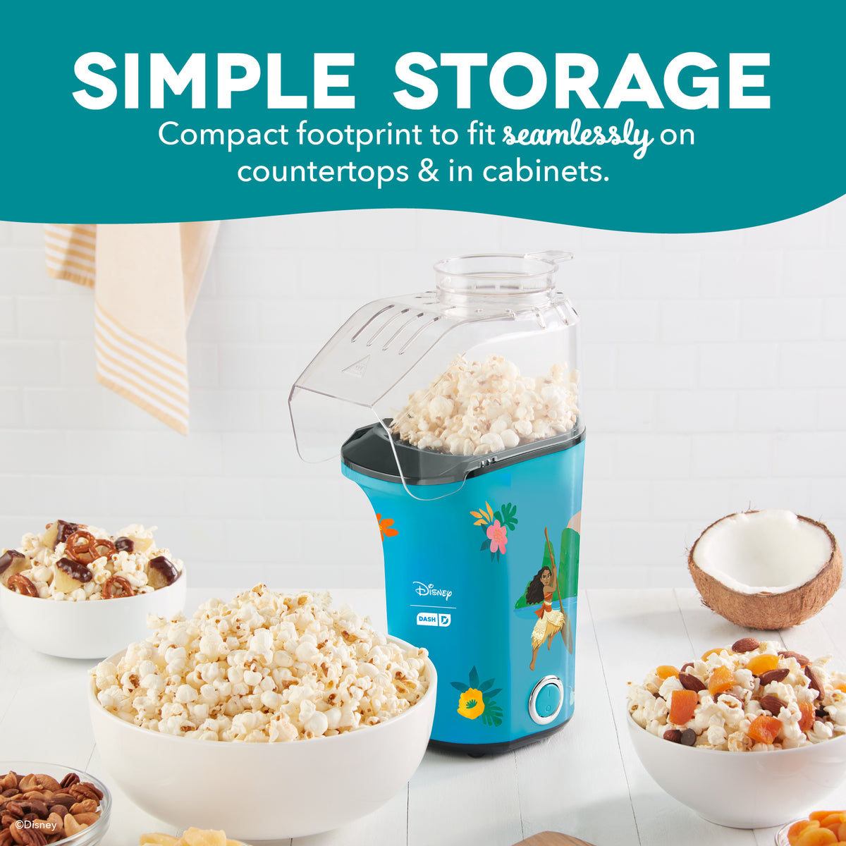 Blue popcorn maker with Disney characters, clear top chamber filled with popcorn, surrounded by bowls of popcorn and toppings