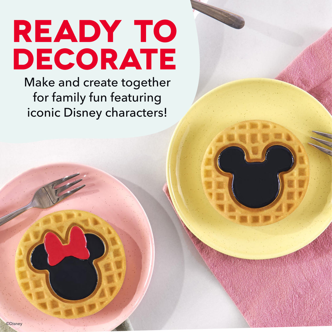 Two waffles with Mickey and Minnie Mouse shapes on pink and yellow plates with forks.