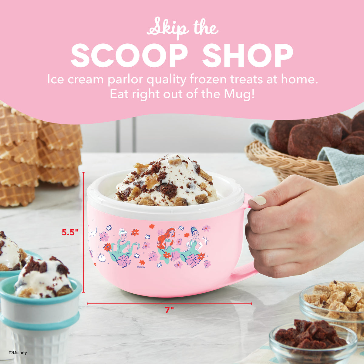 Pink mug-shaped ice cream maker with Disney character graphics, held in hand, filled with ice cream topped with cookie crumbl