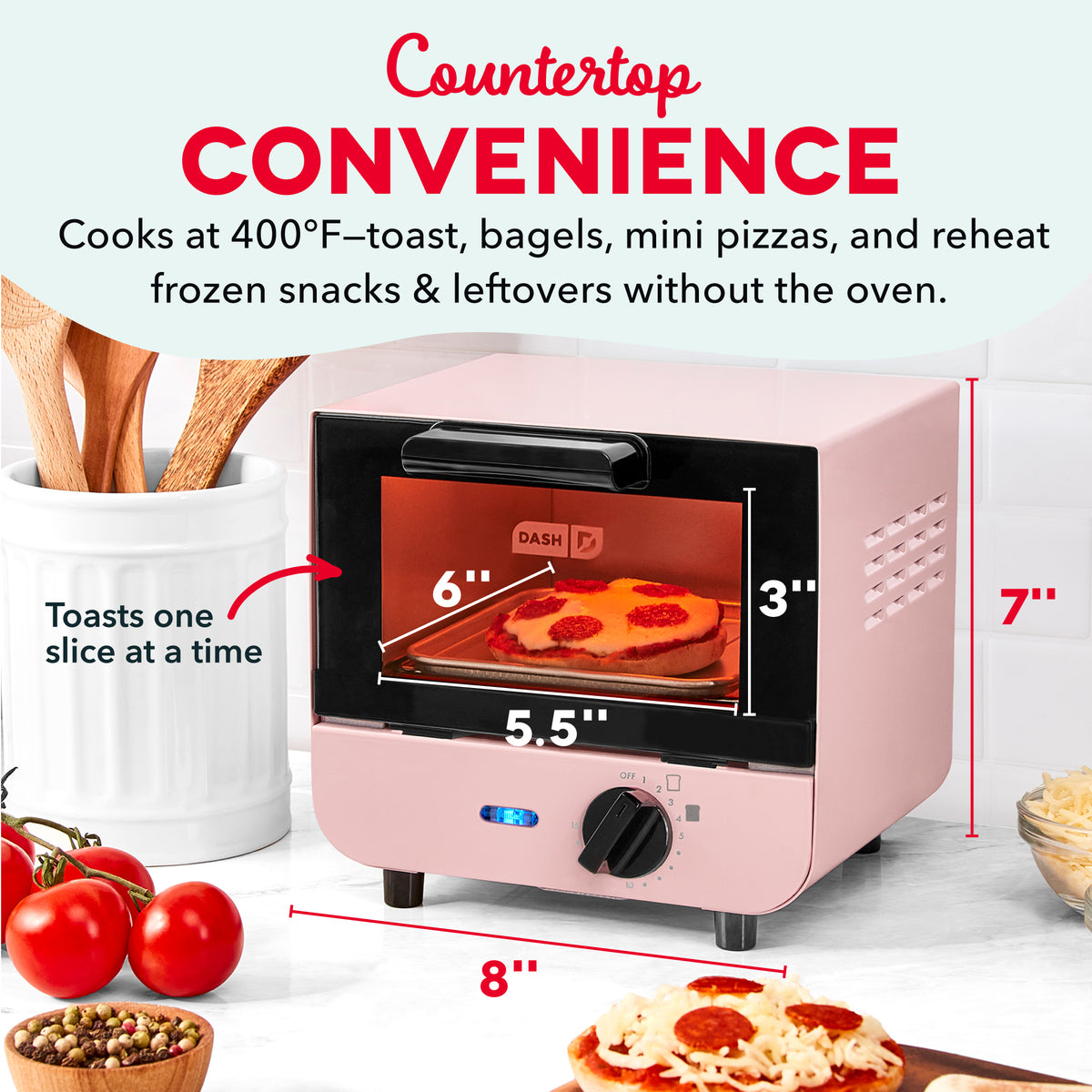 Pink and black mini toaster oven with open door displaying pizza inside, surrounded by tomatoes, utensils, and prepared foods