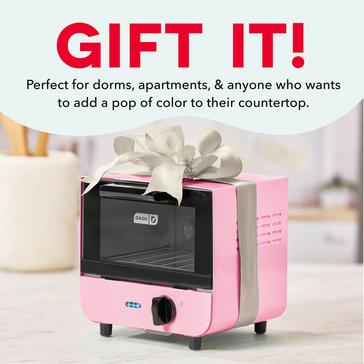 Pink and black compact toaster oven with control dial and gray ribbon bow on countertop.