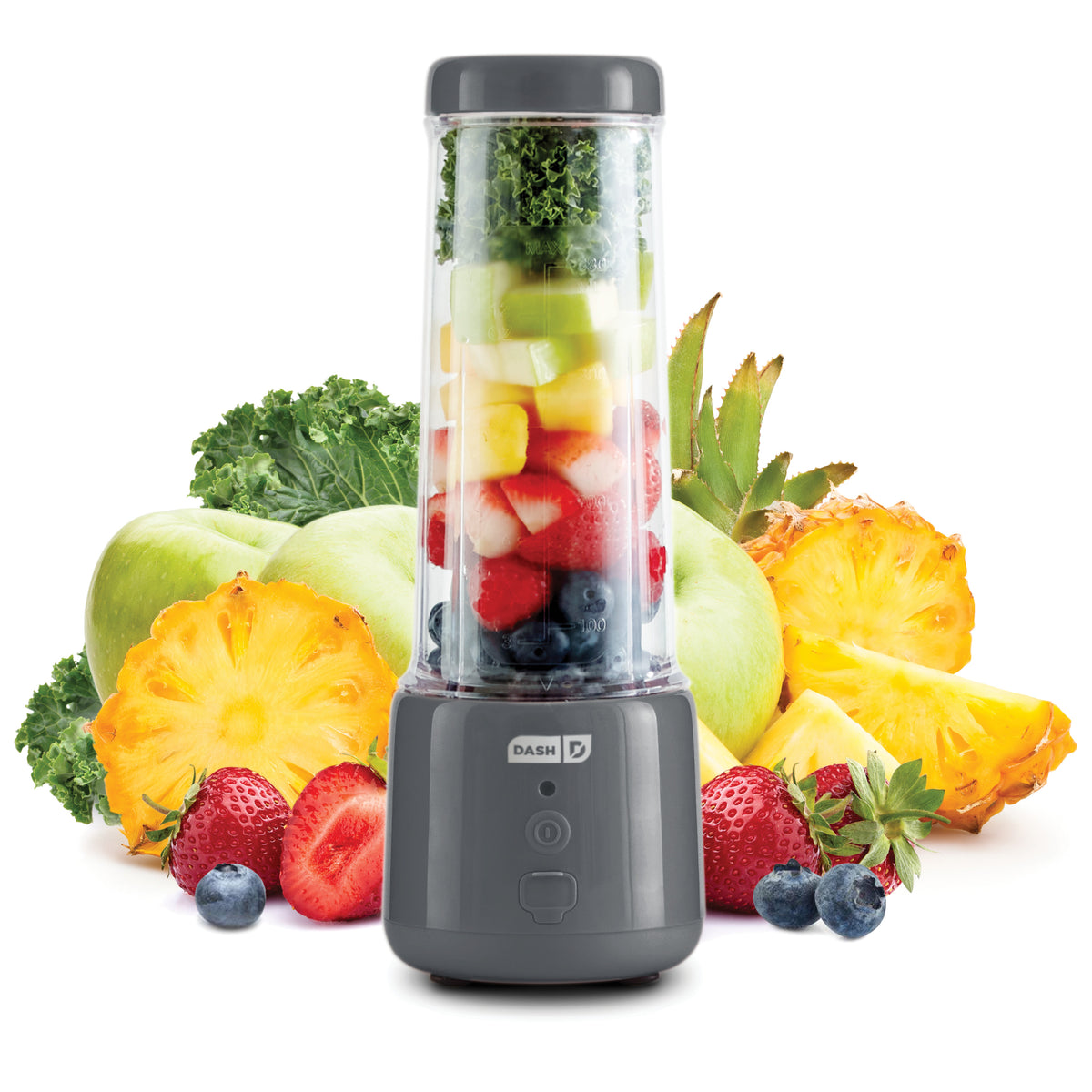 Compact blender with dark gray base and clear pitcher containing layered fruits and greens, surrounded by fresh produce.