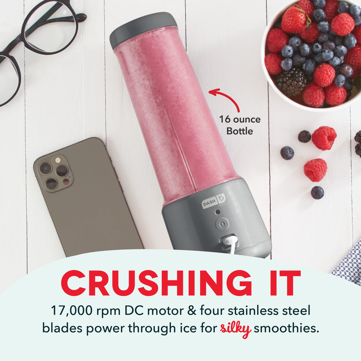 Pink portable blender with gray base, 16 ounce bottle, shown with smartphone, berries, and glasses on white surface.