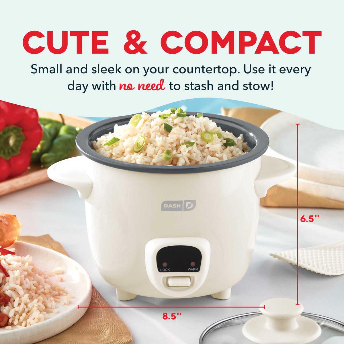 White mini rice cooker with dark gray lid, cook and warm buttons, surrounded by rice, vegetables, and kitchen items on counte