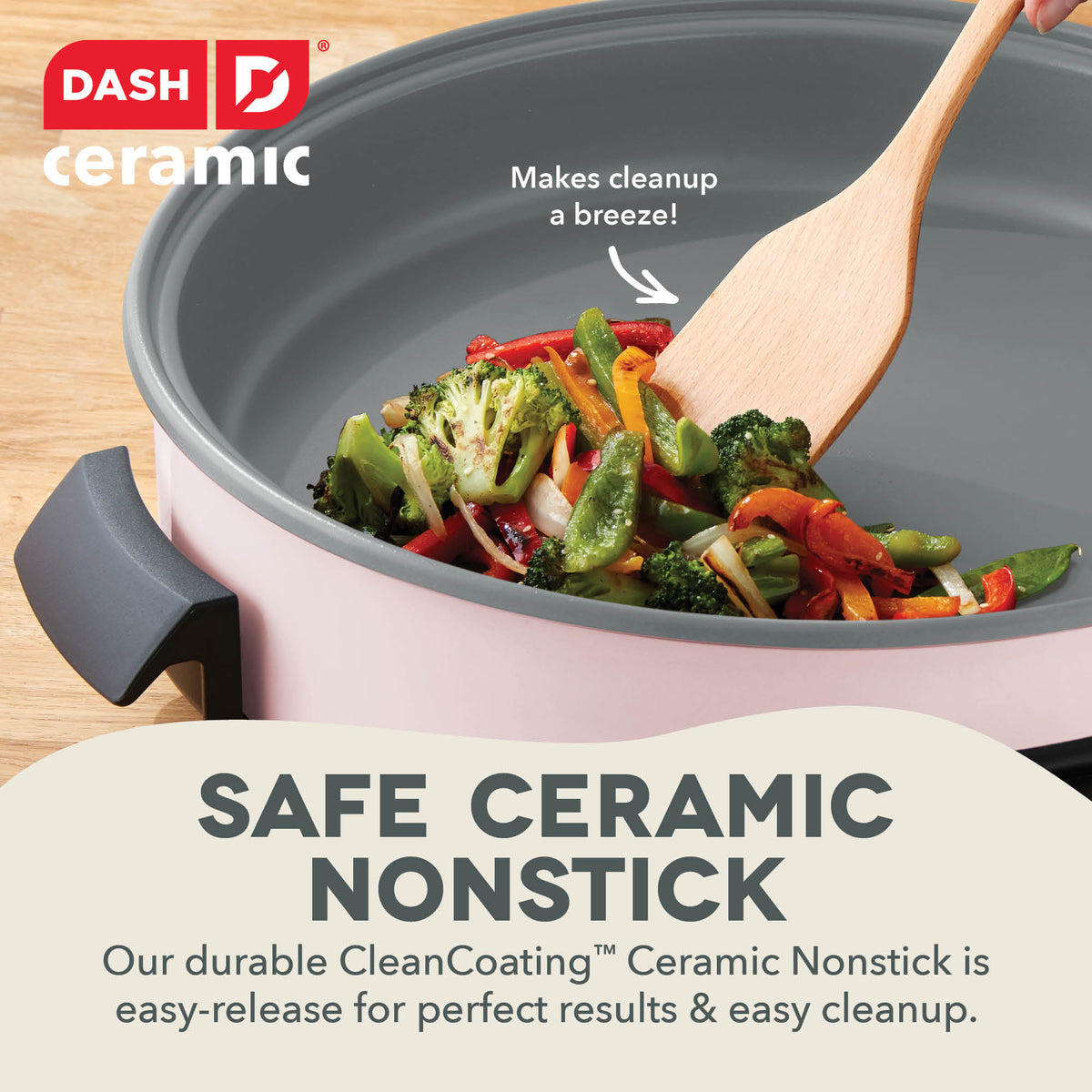 Pink ceramic skillet with gray nonstick interior, wooden spatula, and sautéed broccoli and red peppers inside.