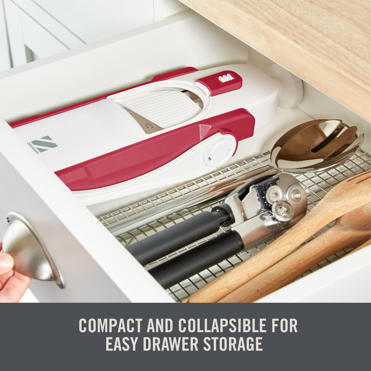 Red and white mandoline slicer with safety guard stored in kitchen drawer with other utensils.